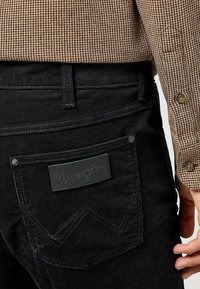 Zwarte corduroy broek met een gestikt zigzagontwerp op de achterzakken, voorzien van een leren Wrangler logo-label en textielstof.