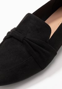 Mocassino in suede nero con dettaglio a fiocco arricciato sulla parte anteriore, texture liscia, punta arrotondata e design minimalista.