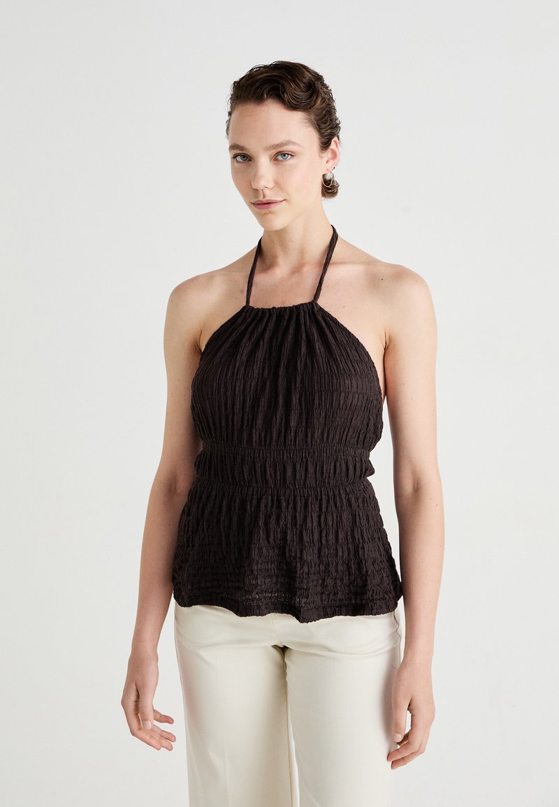 Crni halter top s teksturiranim, nabranim dizajnom i okupljenim strukom. Ima tanke naramenice i valoviti rub, u kombinaciji s krem hlačama.
