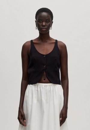 Zwarte cropped top met een ronde halslijn, twee knopen aan de voorkant en brede bandjes, gecombineerd met een vloeiende witte rok. Glad textuur van de stof.