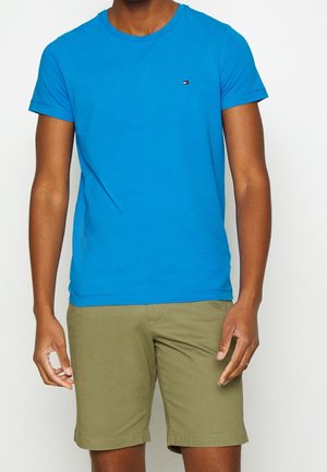 Camiseta de algodón azul con cuello redondo, mangas cortas y un pequeño logo en el lado izquierdo del pecho, combinada con pantalones cortos de color verde oliva.