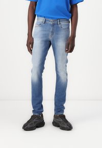 Jeans de mezclilla azul claro con un corte ajustado, textura desgastada, diseño de cinco bolsillos y costuras en contraste. Combinados con zapatillas deportivas negras.