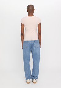 Lichtroze getailleerd T-shirt, korte mouwen, gecombineerd met losse blauwe jeans. De schoenen zijn crèmekleurig met bruine zolen. Eenvoudig ontwerp, geen patronen.