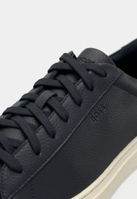 Zapatillas de cuero azul marino oscuro con cordones planos, superficie texturizada y un branding sutil. Presentan una suela de color crema para el contraste.