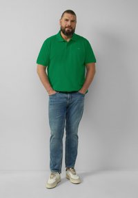 Zielona koszulka polo, krótki rękaw, z kołnierzykiem. Noszona z jasnoniebieskimi dżinsami i białymi trampkami z beżowymi akcentami. Prosty i swobodny design.