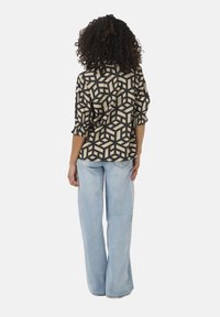 Schwarz-beige gemusterte Bluse mit Dreiviertelärmeln, kombiniert mit hellblauen weit geschnittenen Jeans, die einen lässigen Sitz und einen strukturierten Stoff zeigen.