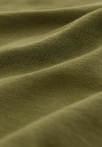 Olīvu zaļš audums ar gludu tekstūru, ar krokām un grumbām. Materiāls izskatās mīksts un līdzīgs kokvilnai, ar smalku adījumu rakstu.