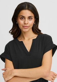 Top nero con scollatura a V e maniche corte arrotolate. Realizzato in un tessuto liscio con una vestibilità rilassata, caratterizzato da cuciture minime e senza fantasie.