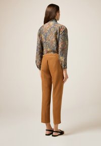 Kwiatowa bluzka w niebieskim kolorze, z bufkami i wysokim kołnierzem. Brązowe zwężane spodnie z miękkiego materiału z pasem. Czarne sandały.