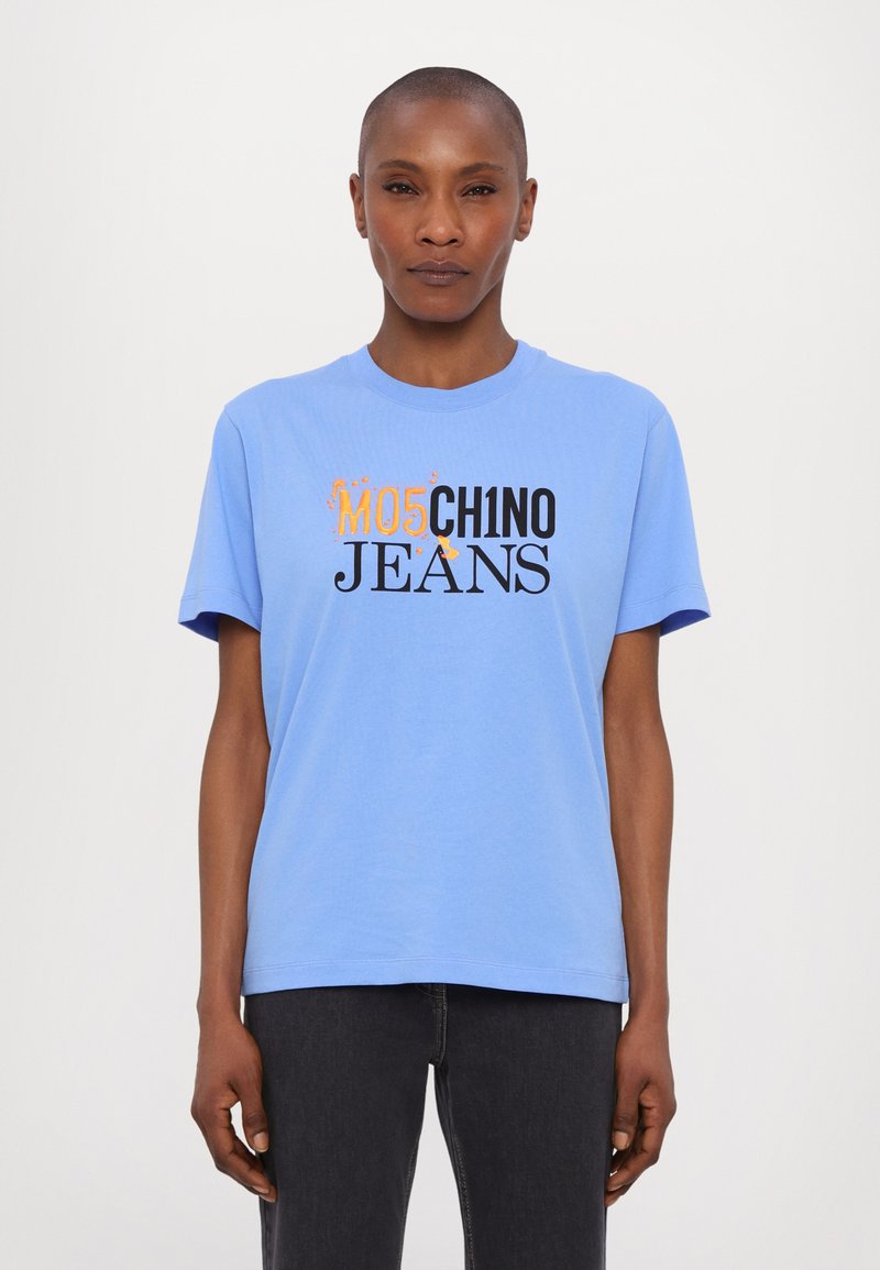 Gaiši zils kokvilnas T-krekls ar īsām piedurknēm, kurā ir pievilcīgs melns un oranžs uzraksts "MO5CH1NO JEANS" uz krūtīm.