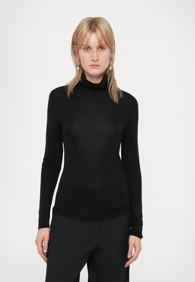 Chemisier noir à manches longues avec col montant, en tissu léger et transparent. Présente une coupe ajustée et une silhouette élancée, associé à un pantalon noir.