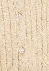Beige stickad tyg med vertikalt ribbat mönster och två genomskinliga blomformade knappar sydda i en vertikal rad.