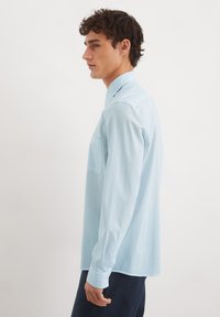 Lichtblauw langemouwen shirt met een gestructureerd ruitpatroon, een enkele borstzak en knoopmanchetten. Eenvoudig, getailleerd model, minimalistisch ontwerp.