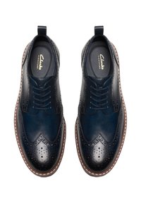 Navy blue leather brogue shoes with wingtip design, decorative perforations, and brown rubber sole. Features logo inside and pull tab.