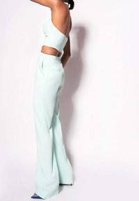Mátově zelený dvoudílný outfit obsahující top s krátkým rukávem a asymetrickým designem a kalhoty s vysokým pasem. Hladká tkanina s širokými nohavicemi.
