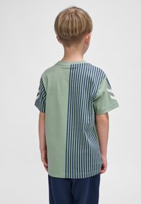 T-shirt en coton vert avec un motif rayé vertical bleu marine sur un côté, à manches courtes et à encolure ronde.