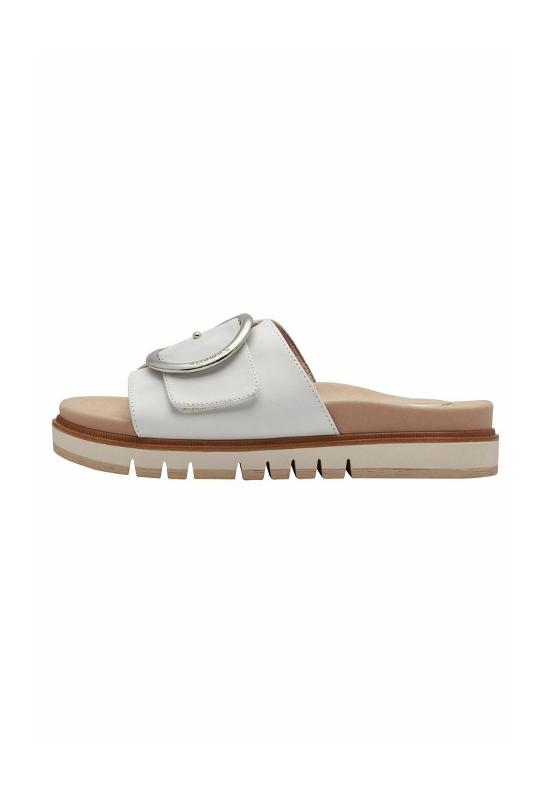 White slide sandal with a rounded toe, featuring a decorative flap and metal accent. Thick, textured sole in contrasting tan and white colors.