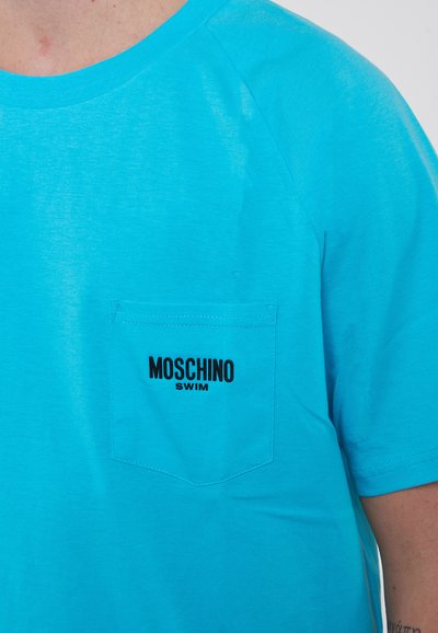 T-shirt in cotone turchese con maniche corte, scollatura rotonda e taschino sul petto con la scritta "MOSCHINO SWIM" in testo nero.