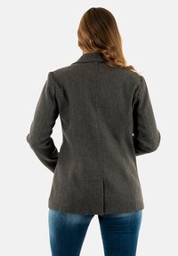 Blazer grigio in lana con vestibilità su misura, caratterizzato da colletto a scollo, dettagli di cucitura sottili e una texture liscia, abbinato a jeans di denim blu.