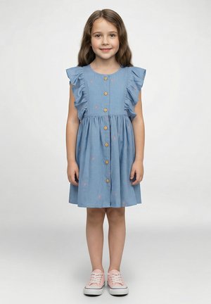 Hellblaues Baumwollkleid mit Rüschenärmeln, angesetzten Knöpfen vorne und kleinen Regenbogenmustern. Kombiniert mit rosa Sneakern.