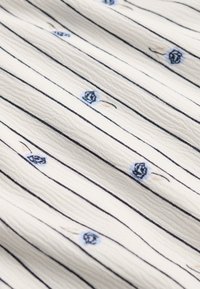 Hvidt stof med tynde lodrette sorte striber og små blå blomstermotiver spredt over overfladen.