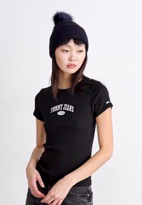 T-shirt nera aderente con maniche corte e logo "TOMMY JEANS" in bianco sul petto, abbinata a un berretto di lana nero con pompon.