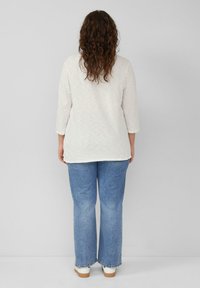 Witte top met driekwart mouwen, gecombineerd met lichtblauwe flared jeans en witte schoenen. De stof lijkt textuur te hebben met een relaxed fit.