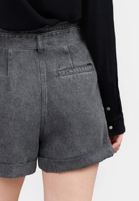 Pantalones cortos de mezclilla gris con dobladillo enrollado, con una cinturilla que tiene pasadores para cinturón y un único bolsillo trasero. La textura parece suave.