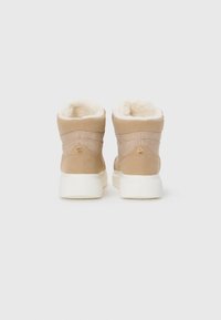 Bottes à chevilles beiges avec doublure en fausse fourrure, en suède, semelles en caoutchouc blanches et détail en logo doré sur le talon.
