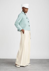 Gaišzilā apgrieztā jaka ar melniem pogām, krējuma krāsas izliektas platās bikses un baltā cepure. Vienkāršs dizains ar gludu tekstūru.