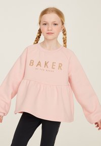 Gaiši rozā sporta krekls ar pepluma dizainu, raglāna piedurknēm un zelta uzrakstu "BAKER". Mīksts, teksturēts audums ar brīvu piegriezumu.