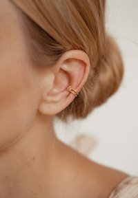 Goldene Ohrcuff mit strukturierten Oberfläche, versehen mit einem kleinen, klaren Edelsteinakzent, der nah am Ohr positioniert ist.