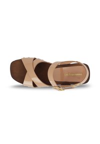 Sandalia de charol beige con suela de madera, con diseño de tiras cruzadas y hebilla en tono dorado para un ajuste ajustable. Punta redondeada.