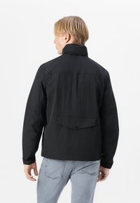 Black lightweight jacket with a high collar, long sleeves, and a back pocket. Made of textured fabric for a relaxed fit.