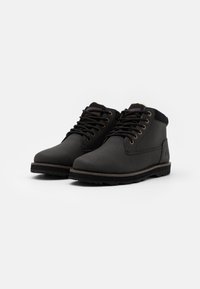 Botas de media caña negras hechas de material sintético texturizado. Cuentan con suelas de goma, ojales de metal y diseño de cordones con forro suave.