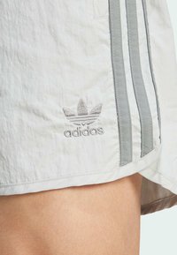 Hellgrauer Sportrock aus strukturierter Stoffqualität, mit drei vertikalen dunkelgrauen Streifen und einem gestickten Adidas-Logo.