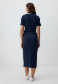 Abito blu navy con maniche corte, colletto e vita aderente. Tessuto morbido, lunghezza al ginocchio, abbinato a sneakers bianche.