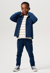 Blå denimskjorta med knäppning, vit randig t-shirt under, matchande blå sweatpants och marinblå sneakers med vita snören.