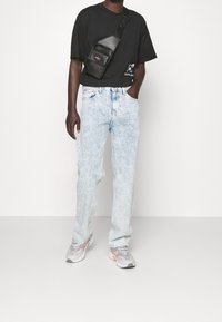 Camiseta negra de manga corta, jeans desgastados de color azul claro, zapatillas grises con acentos naranjas, y un bolso cruzado negro con un bolsillo con cremallera.