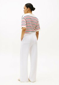 Gestreepte polo in wit, rood en marineblauw, met korte mouwen. Gepaard met luchtige witte linnen broeken met twee achterzakken.