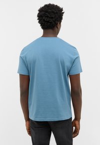 Niebieska bawełniana koszulka z krótkim rękawem i okrągłym dekoltem, o gładkiej teksturze i prostym dolnym wykończeniu, noszona z ciemnymi dżinsami.