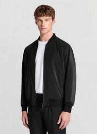 Veste bomber noire en tissu lisse, dotée d'une fermeture éclair frontale, de poignets côtelés et d'une coupe droite. Portée sur un t-shirt blanc.