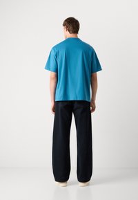 Μπλε βαμβακερό t-shirt με κοντά μανίκια και στρογγυλή λαιμόκοψη, συνδυασμένο με φαρδιούς ναυτικούς παντελόνους και ανοιχτόχρωμα παπούτσια.