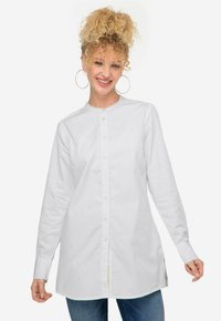 Camicia bianca con bottoni, maniche lunghe, colletto band e spacchi laterali. Realizzata in tessuto liscio con una vestibilità regolare. Design minimalista.