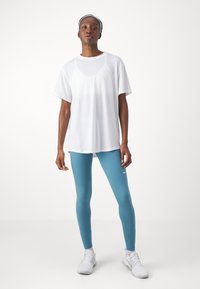 Camisola atlética de manga curta branca combinada com leggins azuis e sapatilhas brancas. Design simples, tecido leve e ajuste elegante.