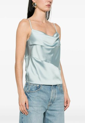 Donna con top in raso azzurro chiaro con spalline sottili e jeans blu a vita alta, accessoriata con grandi orecchini a cerchio dorati.