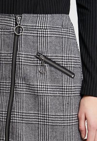 Grå och svart rutmönstrad kjol med sidoficka, texturerat tyg och rund dragkedja.