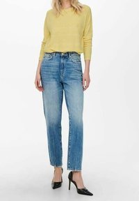 Hellgelb gestreifter Pullover kombiniert mit hoch taillierten blauen Jeans. Die Jeans haben einen geraden Schnitt und leichte Fransen am Saum. Schwarze Absätze.