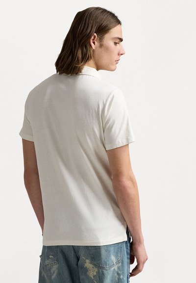 Light beige short-sleeve polo shirt with a soft texture and classic collar, paired with blue distressed jeans.