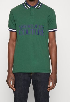 Polo vert avec une patte de boutonnage à trois boutons, doté d'un col et de poignets côtelés bleu marine et blanc. Affiche l'inscription "VERSACE JEANS COUTURE" en lettres majuscules.